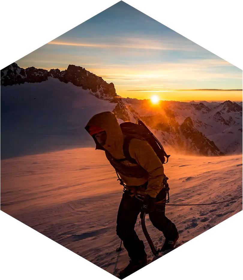 entretien de matériel de montagne, homme équipé qui marche dans la neige dans les montagne avec le soleil couchant sur l'horizon