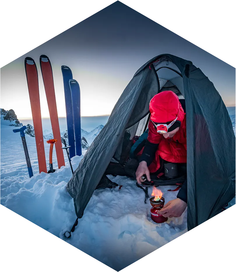 Entretien de matériel outdoor pour domir, homme dans sa tente sous la neige avec des skis plantés à côté